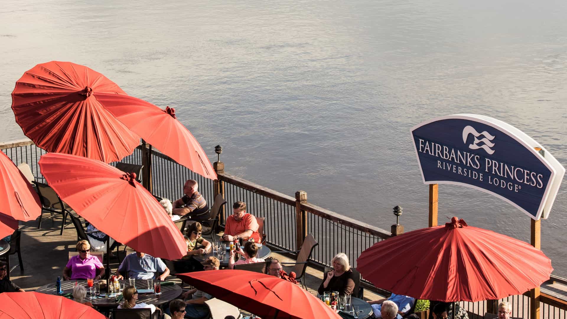 A shot of the Fairbanks Princess Wilder Lodge's outdoor riverside deck with guests enjoying al fresco dining.
