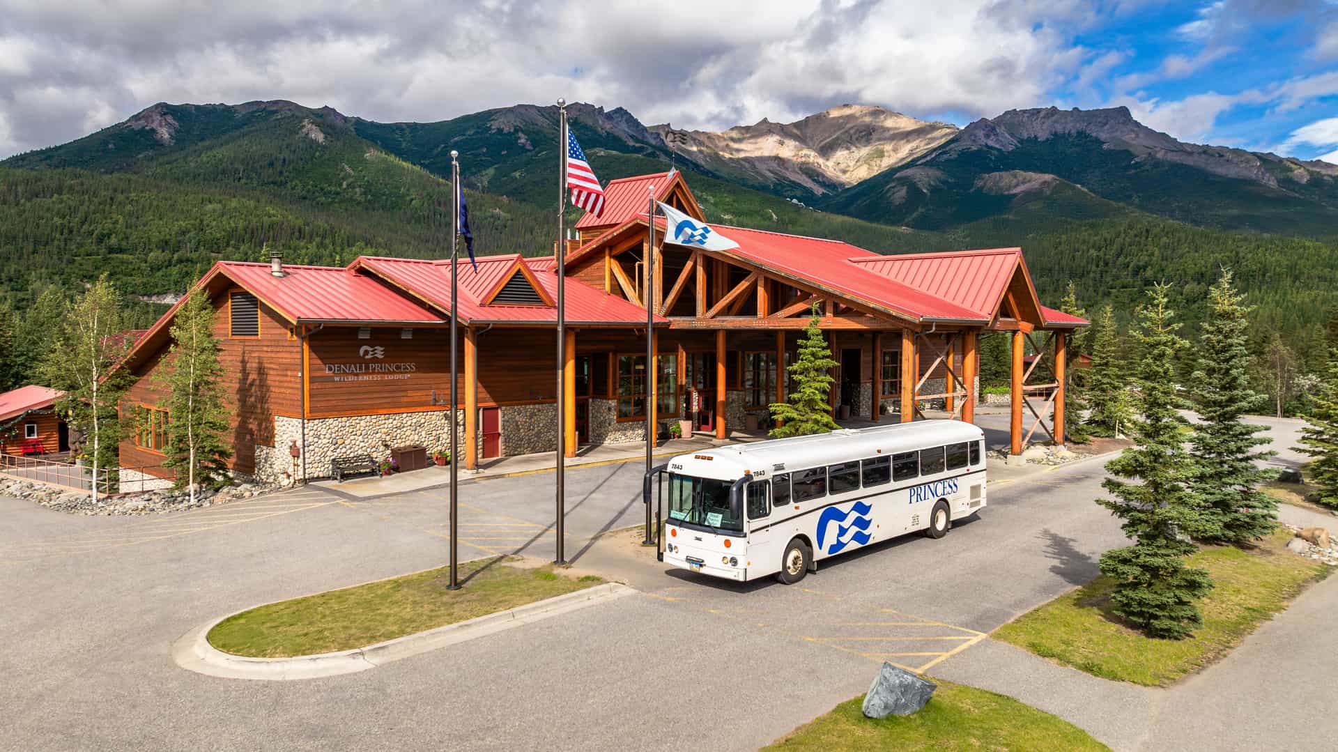Aerial drone shot of Mt.McKinley Princess Wilderness Lodge in Alaska, showing the huge parking lot and entrance of the lodge with a Princess branded motor coach parked out front.