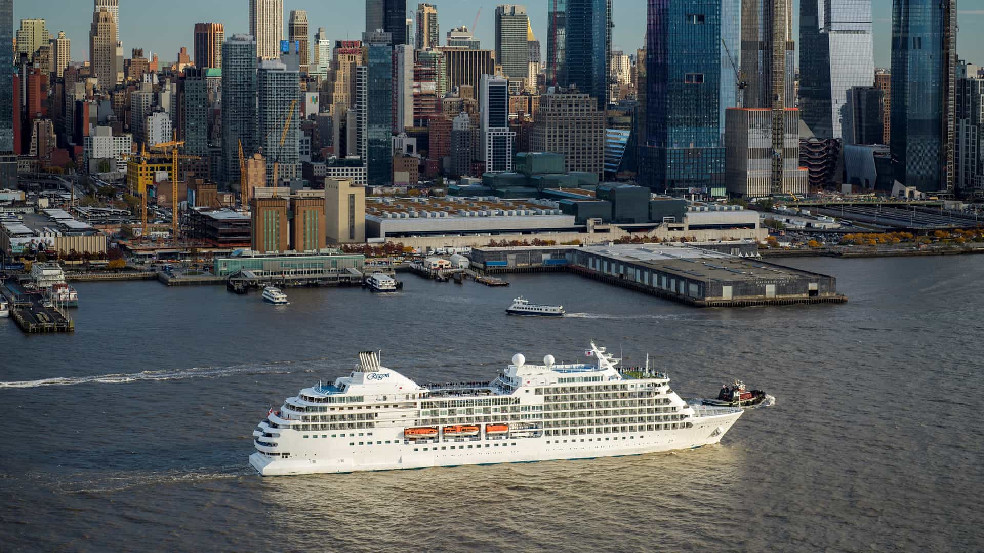 The Regent Seven Seas luxury cruise ship sailing along the Hudson River with the iconic New York City skyline in the background.