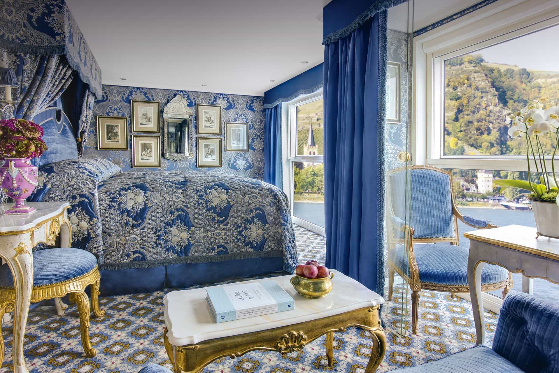A wide view shot of a uniquely styled and lavish stateroom draped in a blue theme onboard a Uniworld river cruise ship.