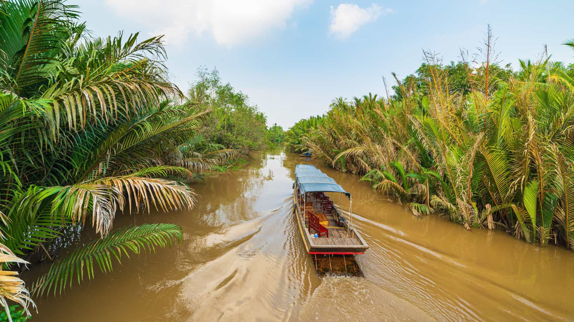 A traditional longtail boat cruising through the lush, tropical waterways of the Mekong River in Vietnam, a scenic highlight of a Viking River cruise through Southeast Asia.