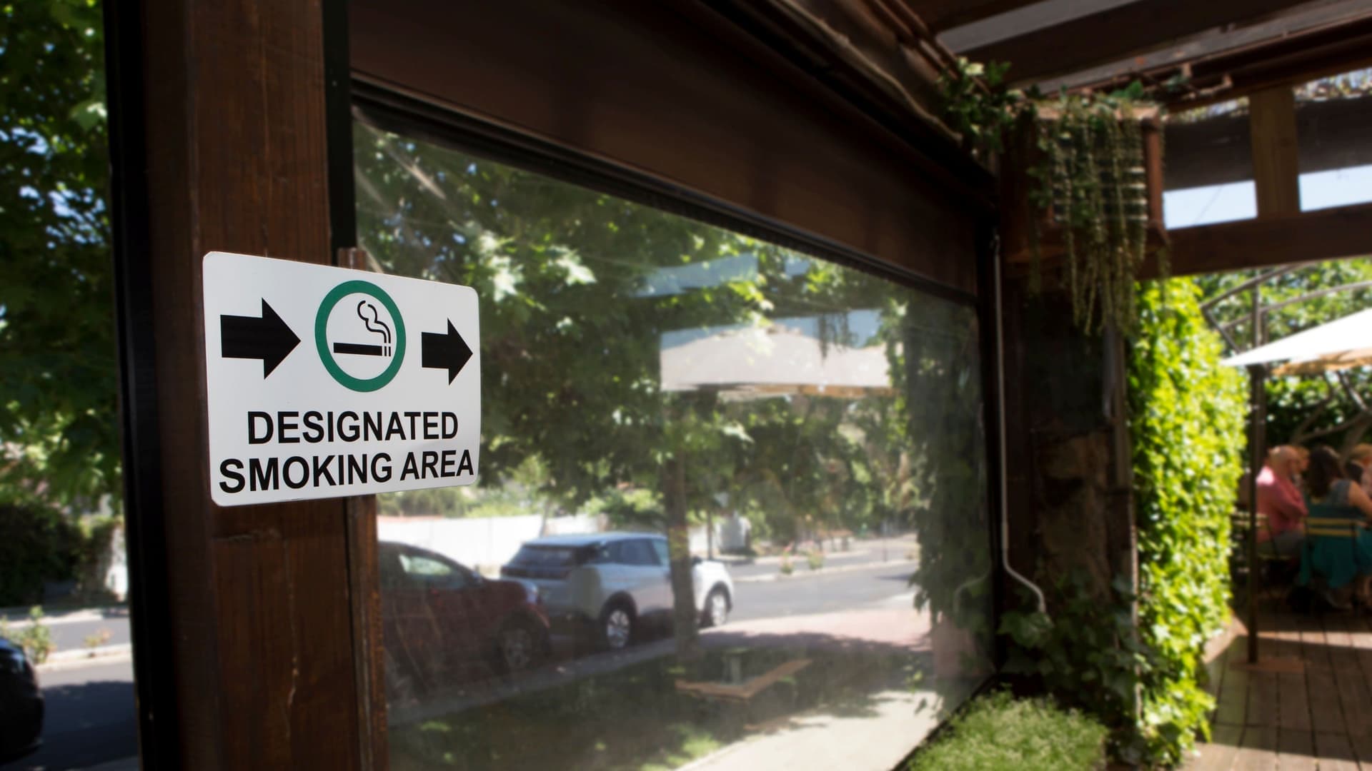 Close up shot of a "Designated Smoking Area" sign hung up and pointed towards an open air patio. 