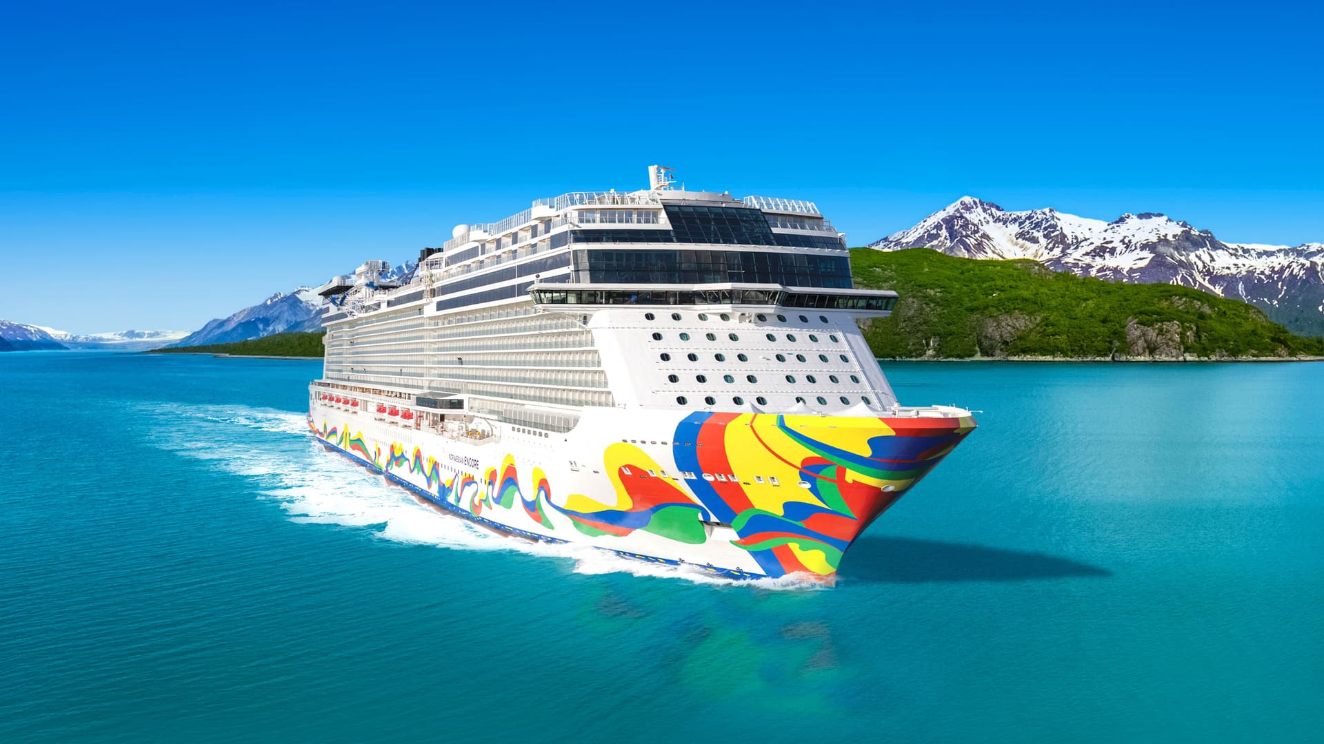 Norwegian Encore sailing past snow-capped mountains in Alaska.