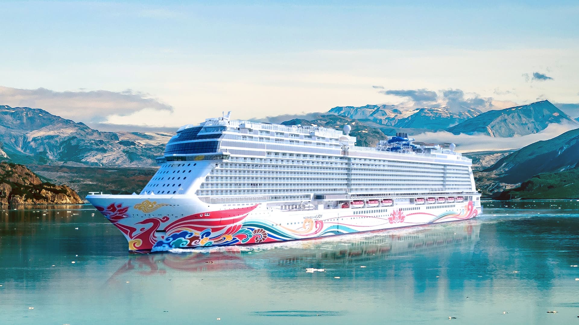 Norwegian Joy sailing with mountains in the background.