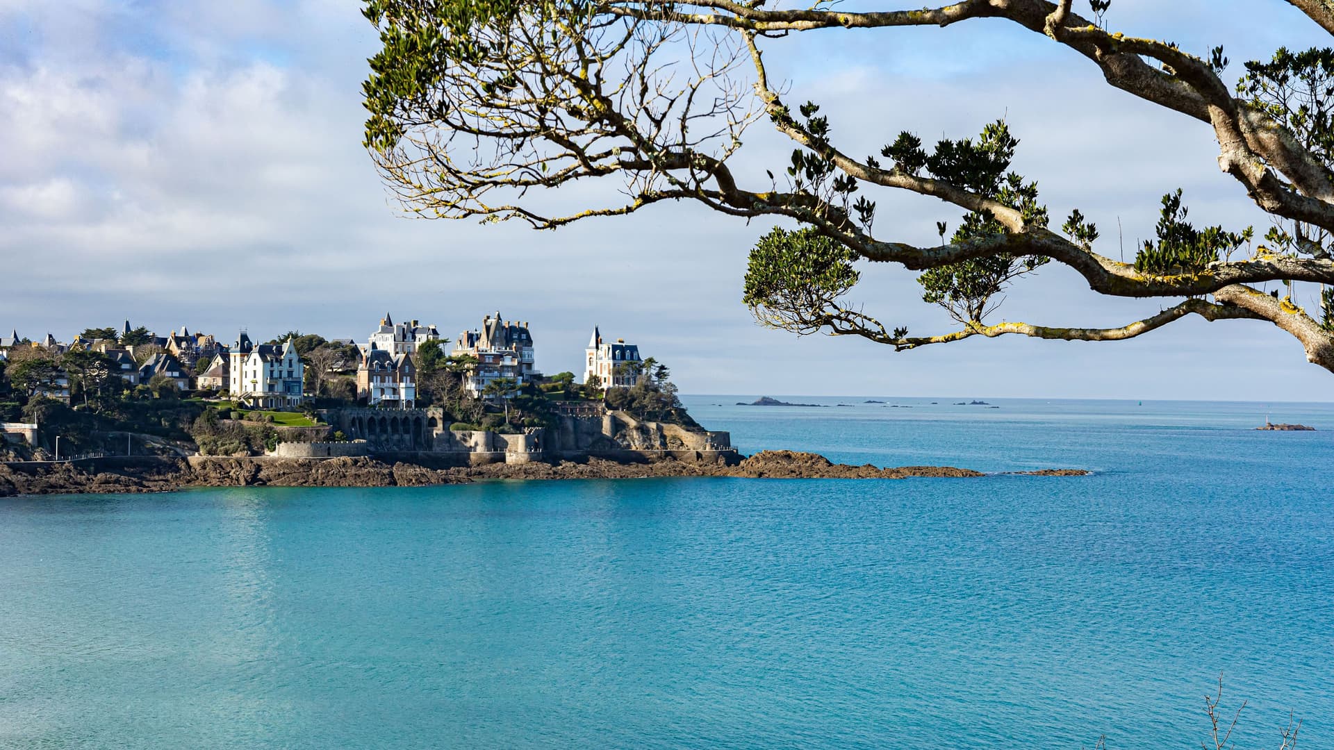 The dramatic coastline of Dinard, Brittany, France, with elegant, historic villas perched on a cliff overlooking the sparkling turquoise waters of the Emerald Coast.