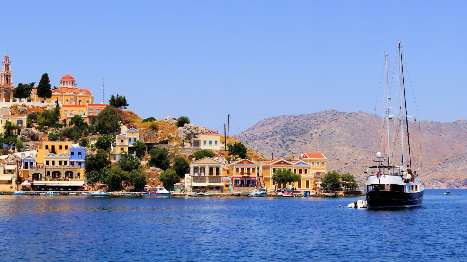 A beautiful yacht anchored in the harbor of Symi Island, Greece, with colorful neoclassical houses built along the scenic hillside.