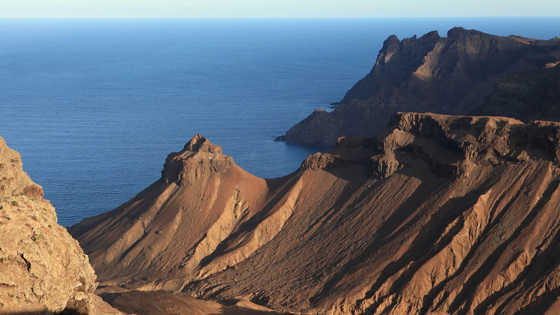 A high-angle view of the rugged, steep volcanic cliffs of Tristan da Cunha, the world's most remote inhabited archipelago, rising dramatically from the Atlantic Ocean.