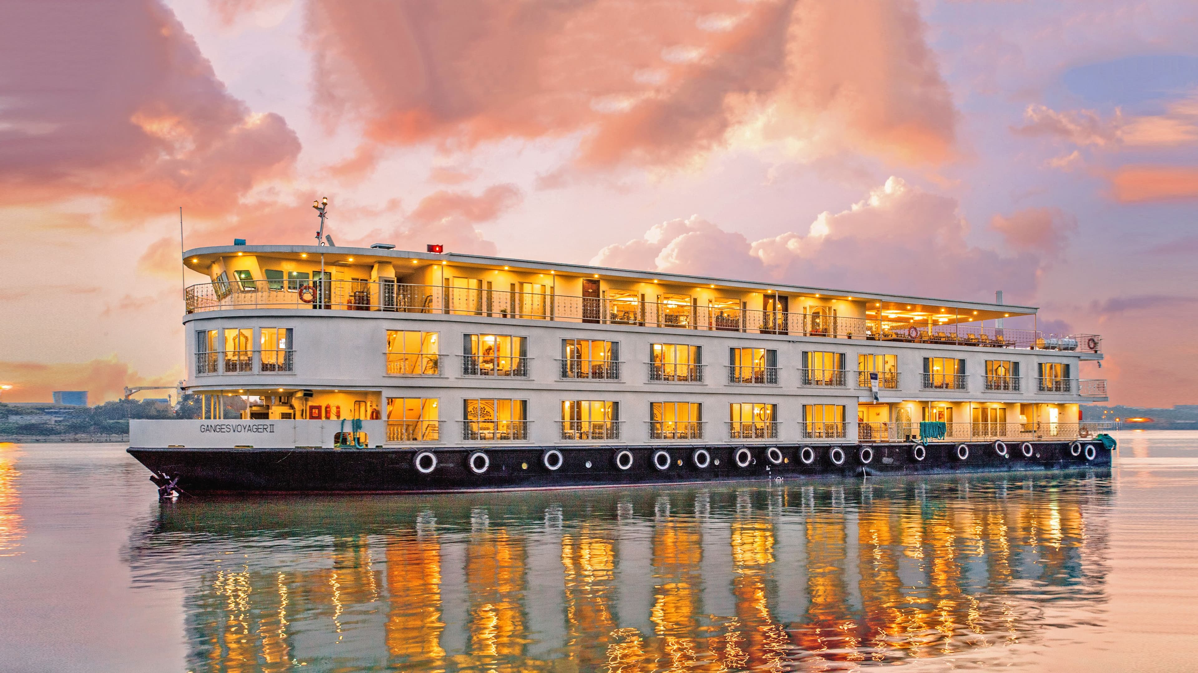 Uniworld's Ganges Voyager II sailing the Ganges under a colorful sunset.