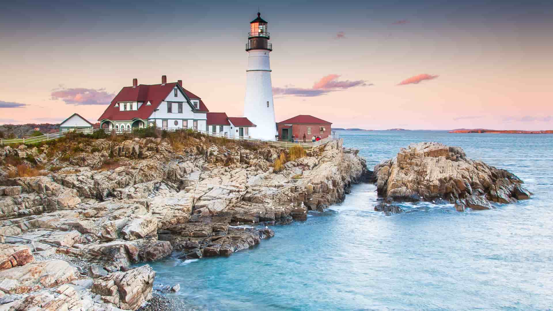 Portland Head Light lighthouse standing against a blue sky in Maine, USA, with rocky coastline below.