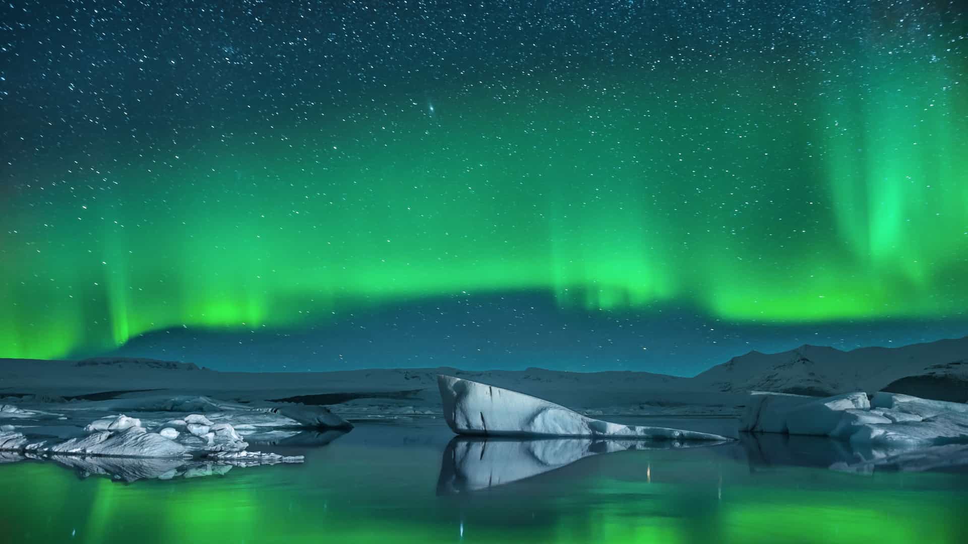 Aurora Borealis and stars glowing above Icelandic icebergs within the Arctic Circle—part of Carnival Cruises’ northern lights journey.