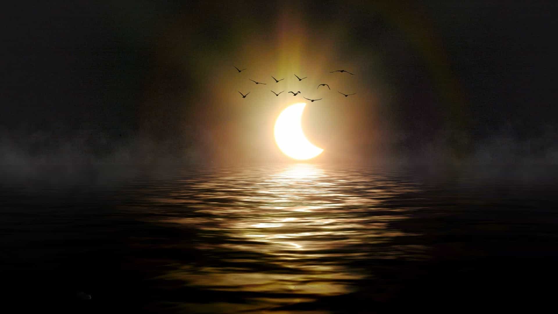 Crescent-shaped sun during a solar eclipse reflecting golden light across the open sea