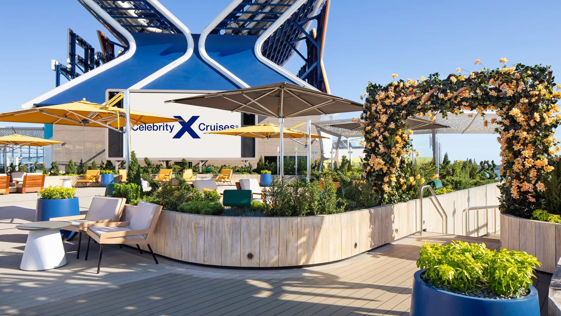 A sunny rooftop garden featuring lush plants, chairs, sun umbrellas, and an overarching decorative floral arch.