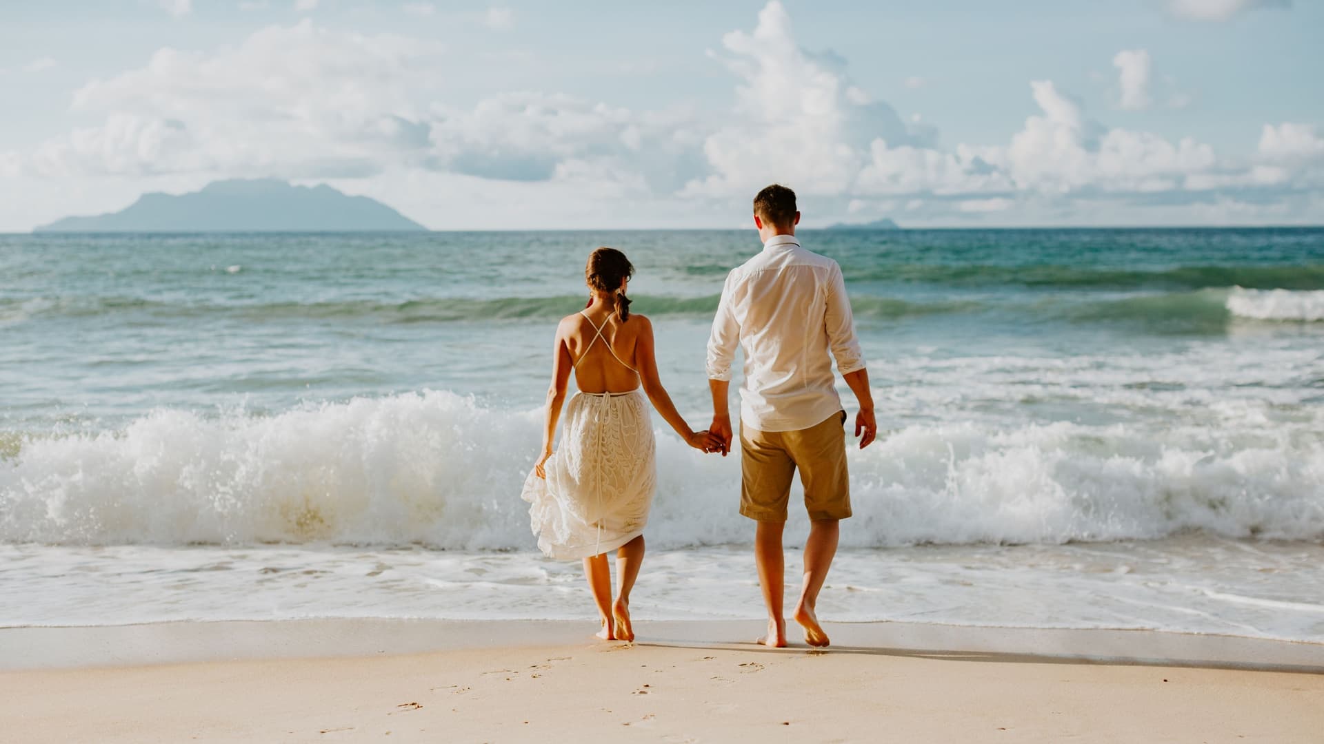 A couple walking along the beach while holding hands during a romantic vacation.