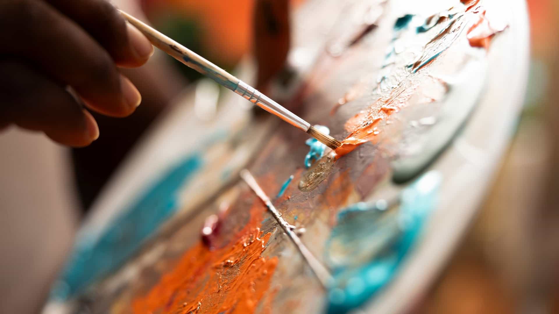 A close-up of an artist mixing vibrant watercolor paints on a palette with a brush. The image features a shallow ceramic palette holding various concentrated colors, capturing the rich detail and creative process associated with fine art, similar to the collections found in museums.