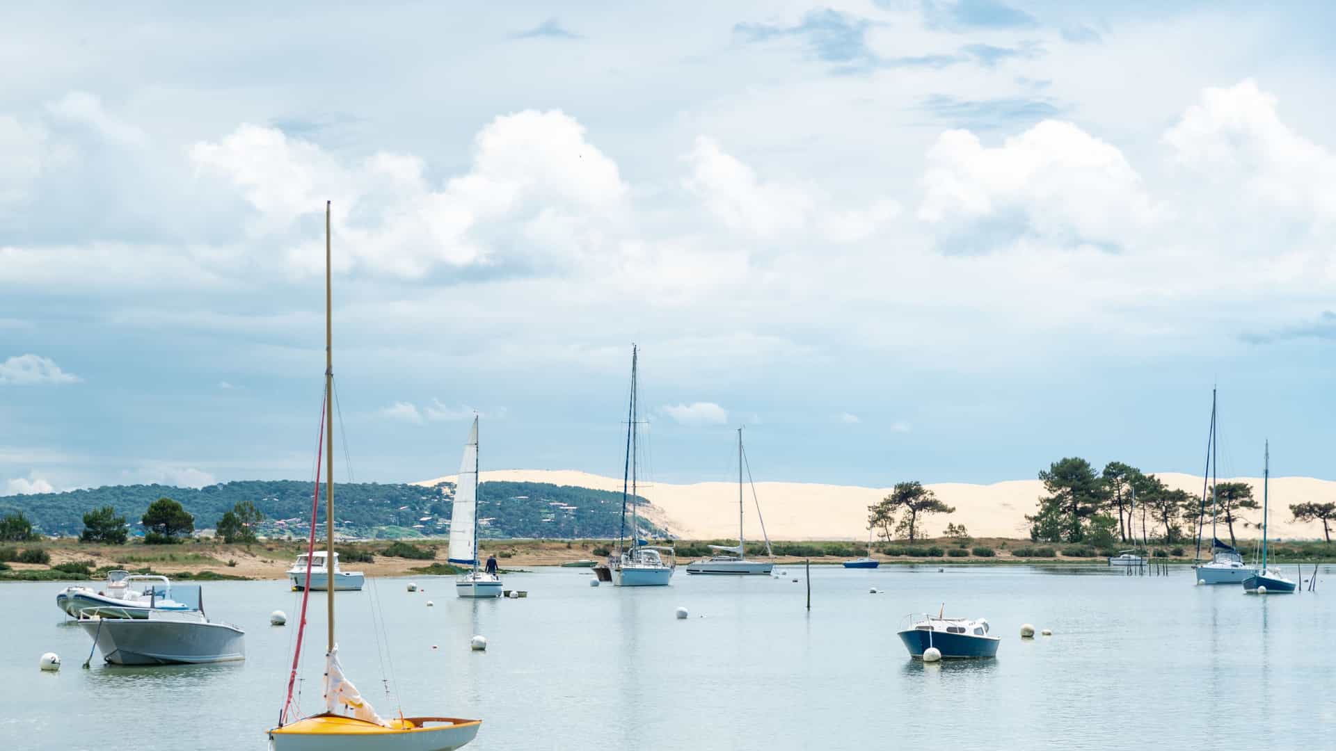 A sweeping panoramic view of the Arcachon Bay (Bassin d'Arcachon) in France, dominated by the distinctive white sand crescent of the Cap Ferret peninsula in the foreground and the vast Atlantic Ocean beyond.