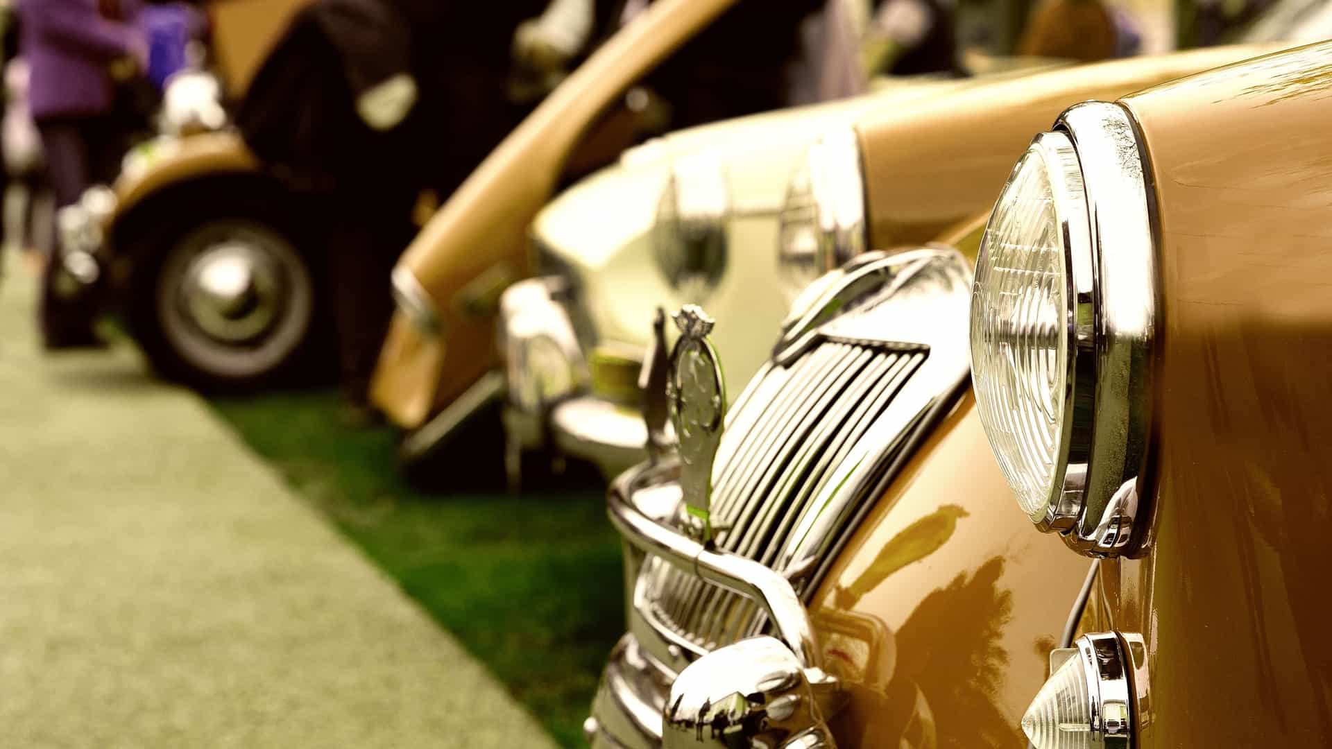 A close up, angled view of a vintage British car, featuring a prominent chrome grille and large circular headlight, parked on a grassy lawn. This vehicle is part of an outdoor exhibition, possibly a show associated with the Dover Transport Museum.