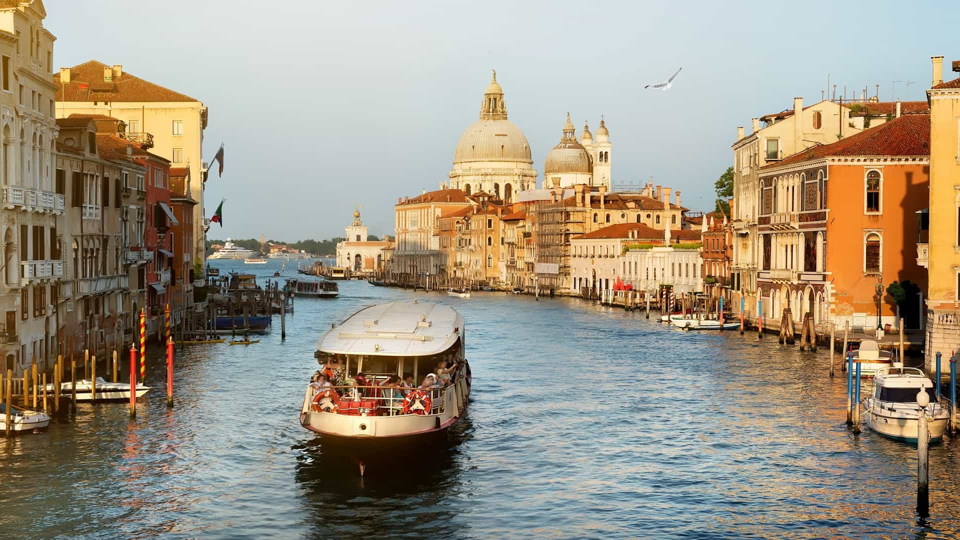 A vaporetto, or water bus, travels down the Grand Canal in Venice, Italy, surrounded by historic buildings and other boats. The image captures the busy waterway and the distinctive Venetian architecture.