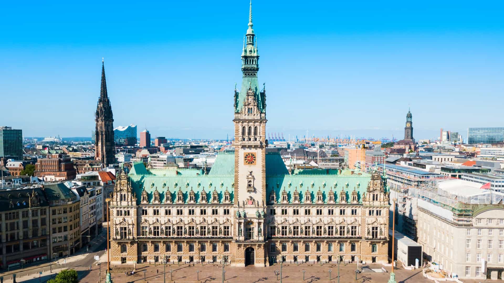 An eye level photograph of the Hamburg City Hall (Hamburger Rathaus), a grand Neo Renaissance building in Hamburg, Germany. The detailed facade is a central focus, showcasing the intricate architectural decorations. The image captures the main tower and the elaborate sculptures that adorn the building's exterior, conveying its historical and governmental significance.