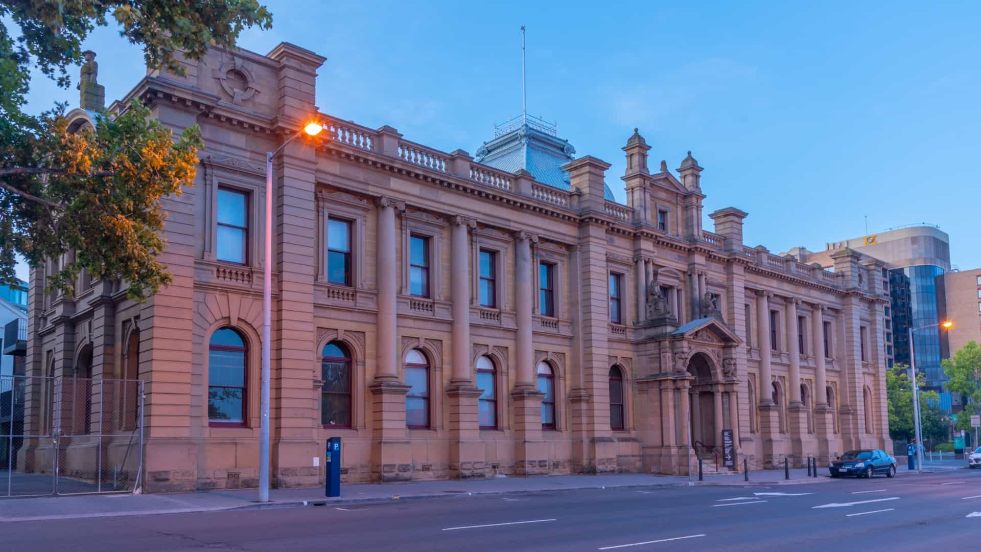 An exterior view of the Tasmanian Museum and Art Gallery (TMAG), located on the historic Hobart waterfront in Hobart, Tasmania, Australia. The image features the museum's complex of heritage buildings, including the sandstone structures that date back to the colonial era, and may also show the modern architectural additions of the redesigned courtyard area.