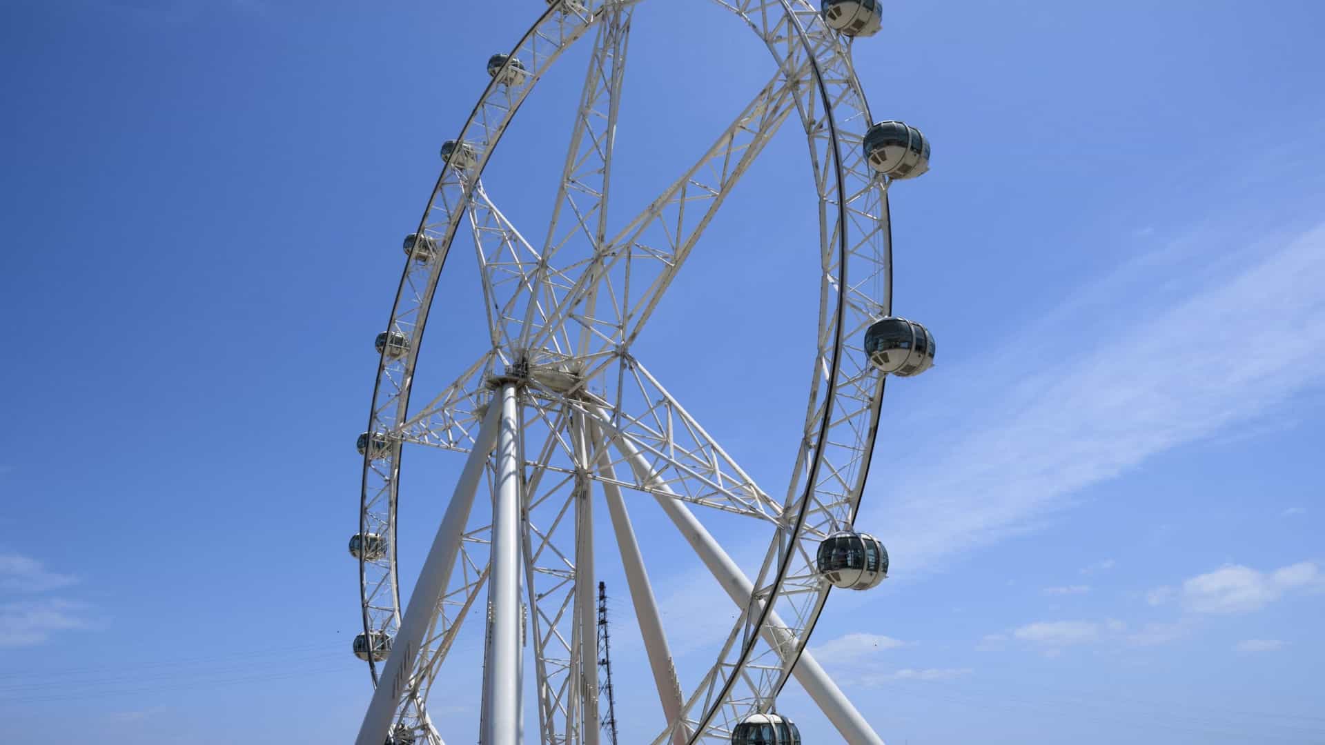A striking, full-frame view of the Melbourne Star Observation Wheel, with its geometric spokes and passenger cabins, standing bright white against a clear, cloudless blue sky.