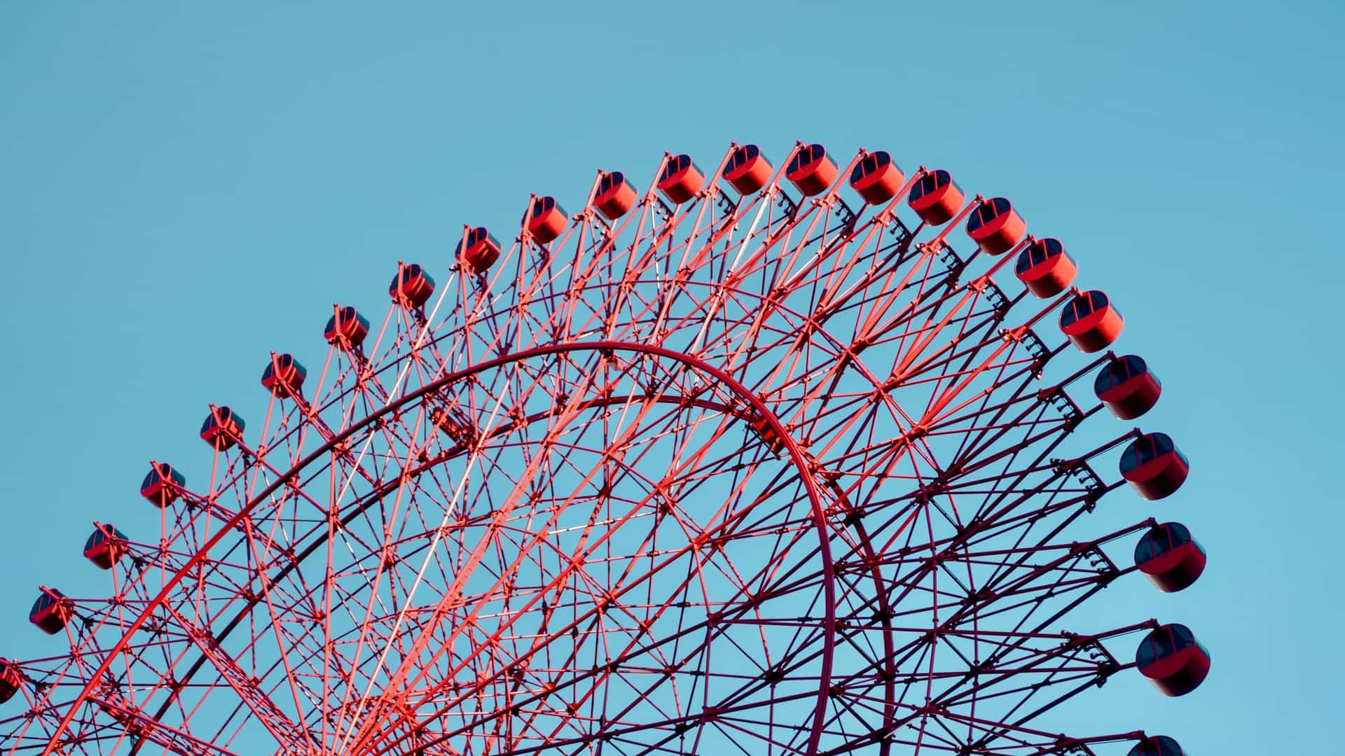 A view of the HEP FIVE Ferris Wheel, a large, bright red Ferris wheel that is built into the top of a modern, glass fronted shopping complex in Osaka, Japan. The wheel is a significant landmark in the city's Umeda district, standing out against the surrounding urban skyline. The photo captures its distinctive design and bright color, which contrasts with the neutral tones of the building it's mounted on.