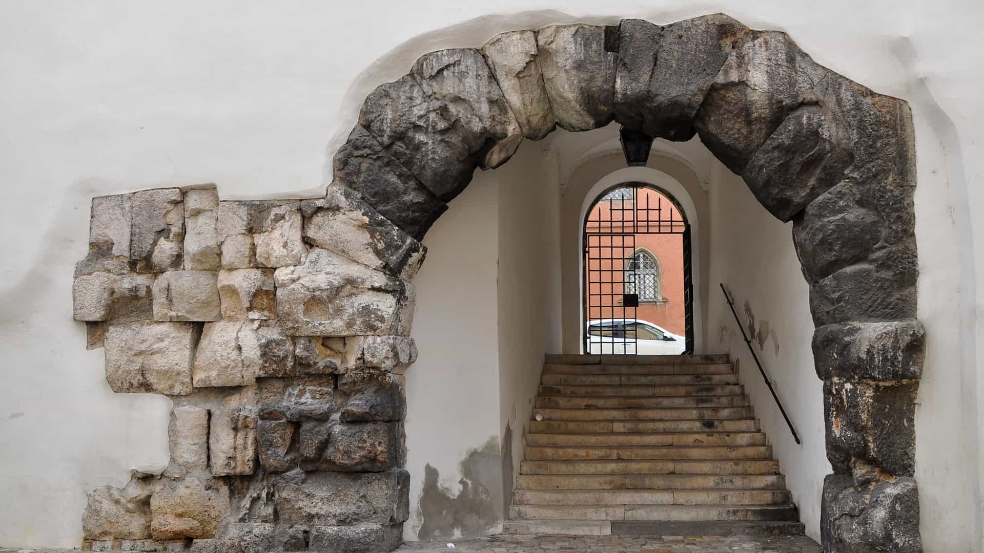 Ancient Porta Praetoria Roman gate in Regensburg, Germany. The large, weathered stone archway stands surrounded by modern city buildings, a relic of the 2nd century fortress.