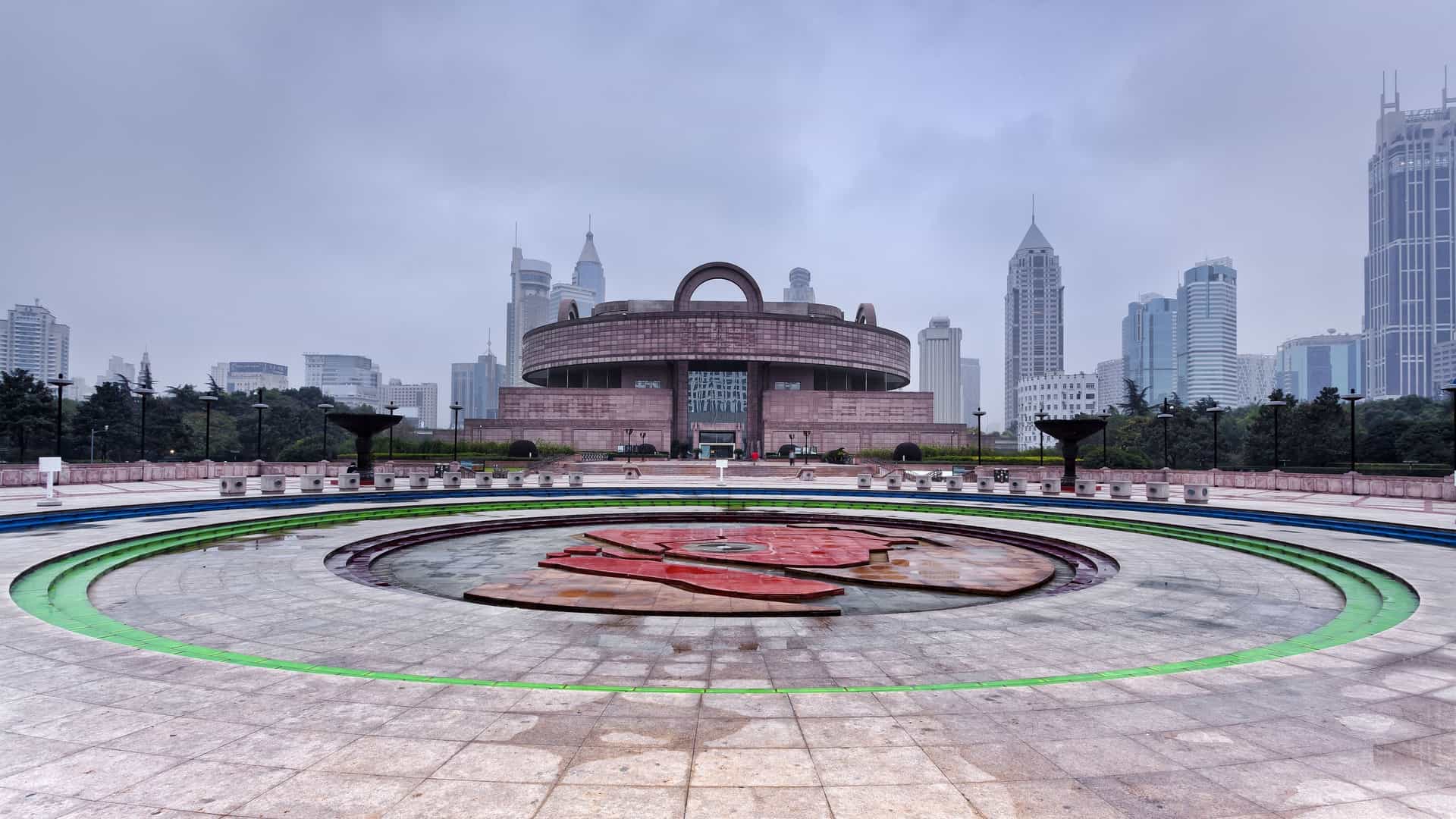 The imposing front view of a famous historical Chinese museum, which is likely the National Museum of China on Tiananmen Square. The architecture is monumental, featuring a massive, symmetrical facade with a long row of classical columns or pillars, and a flag flying prominently at the entrance. The building's design evokes a sense of national importance and historic grandeur.