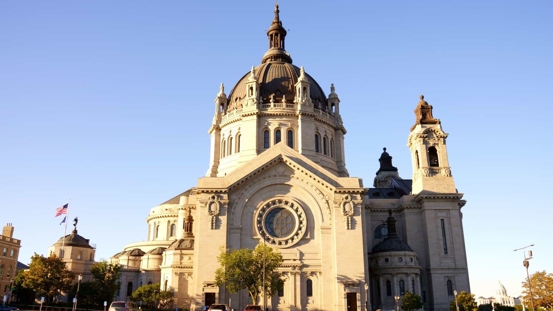 The majestic exterior of the Cathedral of Saint Paul in St. Paul, Minnesota, a grand Roman Catholic cathedral built in the Beaux Arts style, featuring its prominent copper dome and St. Cloud granite facade under a bright sky.