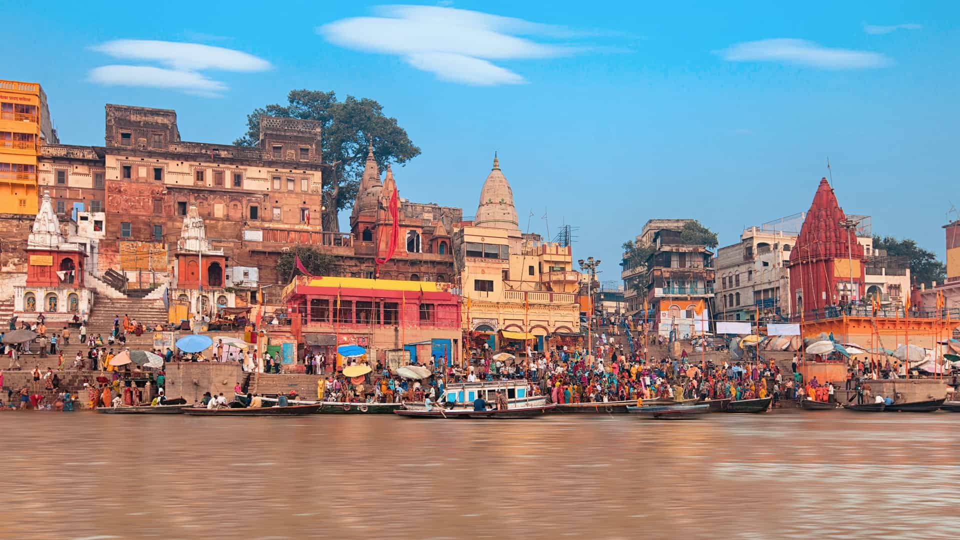 A view of the Ganges River with boats floating and buildings lining the banks.