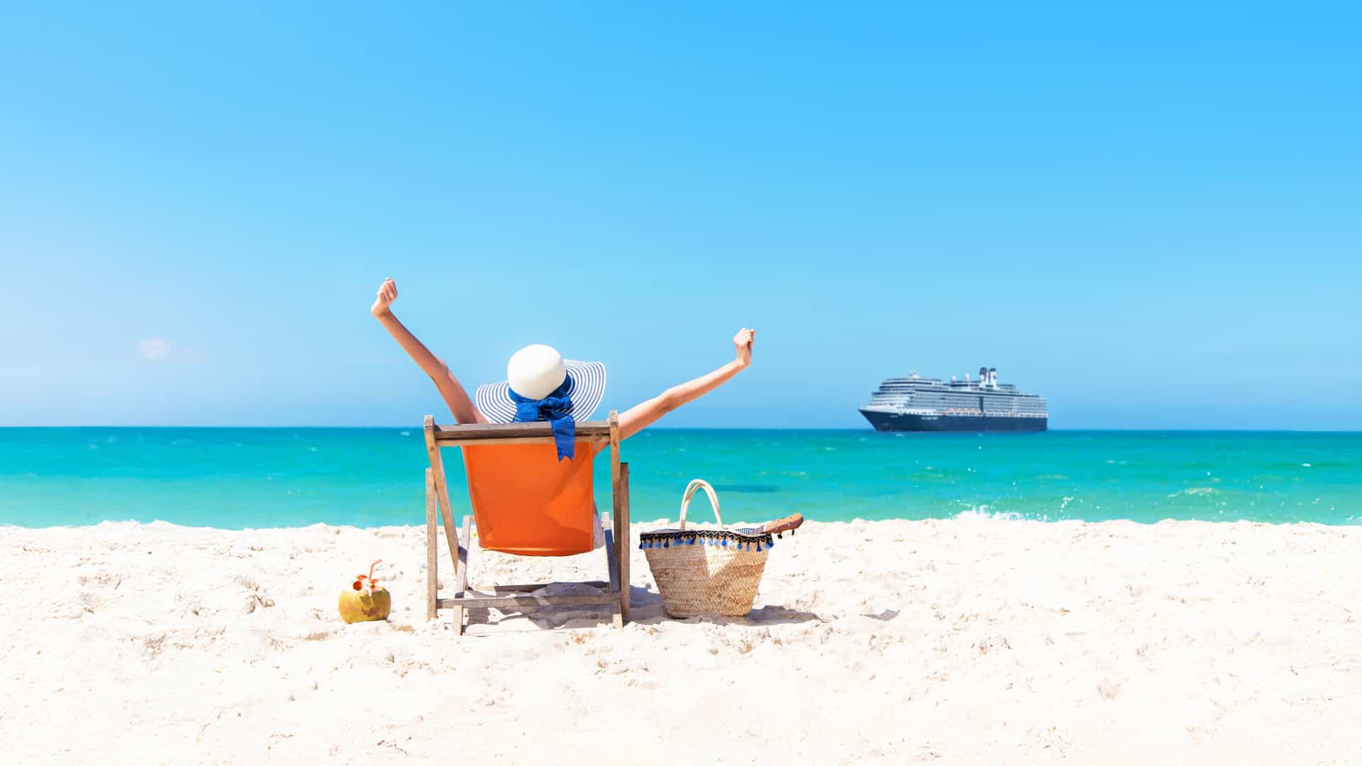 A woman sitting in a beach chair with her arms raised, with a Holland America ship in the background.