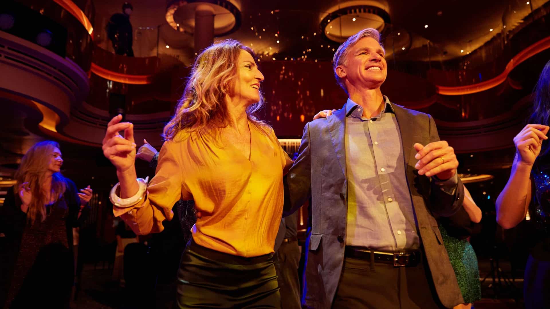 A smiling man and woman on the Holland America Line's Nieuw Statendam ship are dancing at a nightclub, with the man's arm around the woman's shoulder.