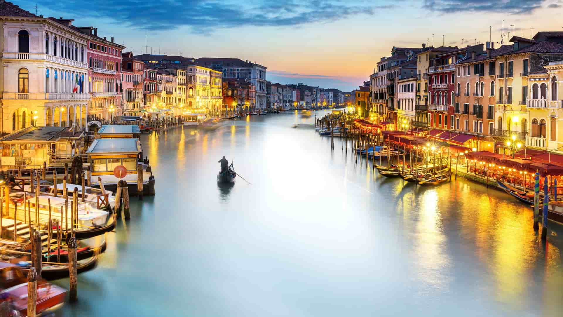 A gondola on the Grand Canal at sunset in Venice, Italy, with warm colors reflecting on the water.