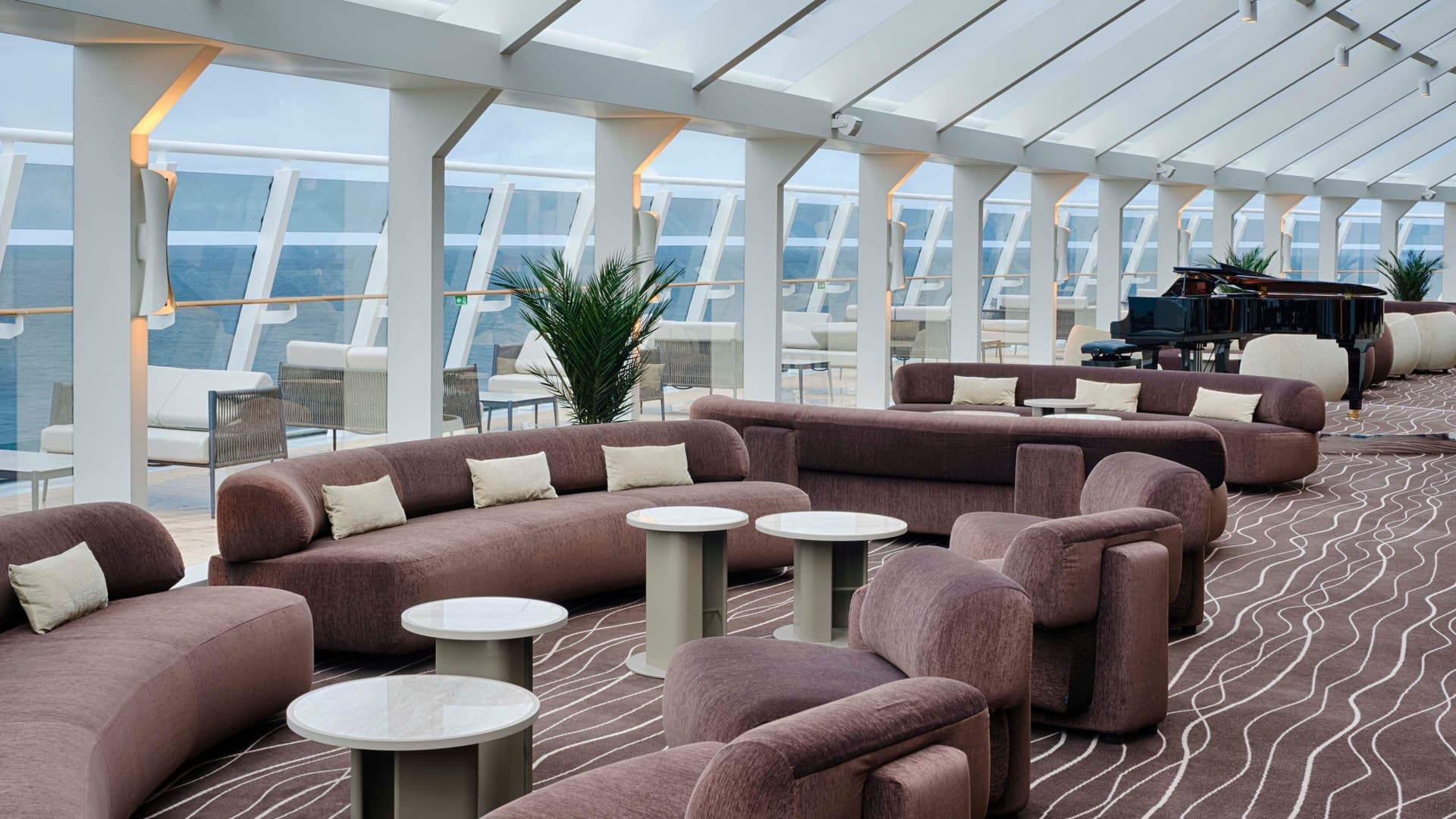 Dusty rose colored sofas in the MSC Yacht Clubs exclusive Top Sail Lounge, featuring mid-century modern decor and floor to ceiling windows.