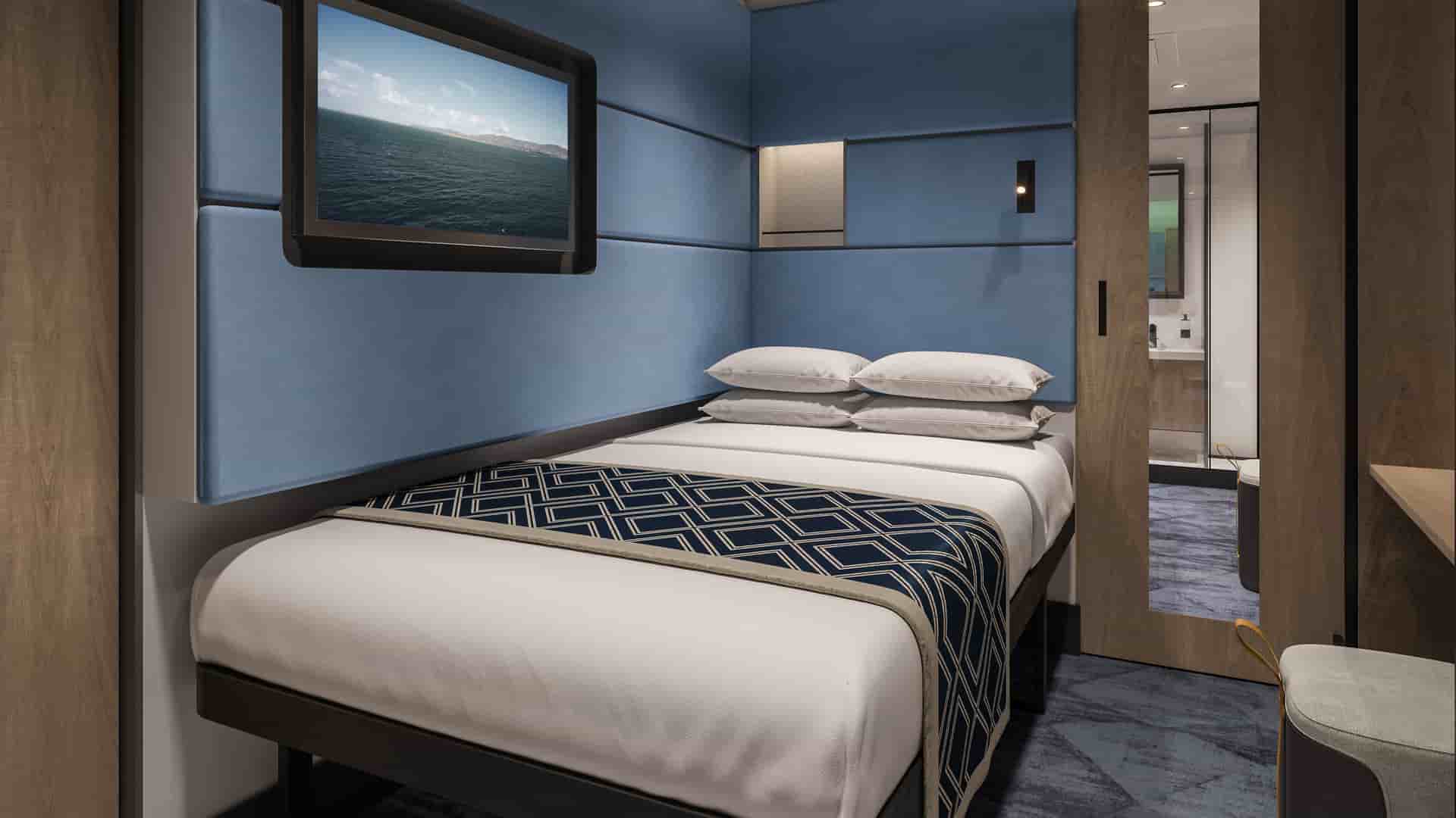 Solo Studio on Norwegian Aura with a bed, blue padded walls, a wall-mounted TV showing an ocean view and wood cabinetry.