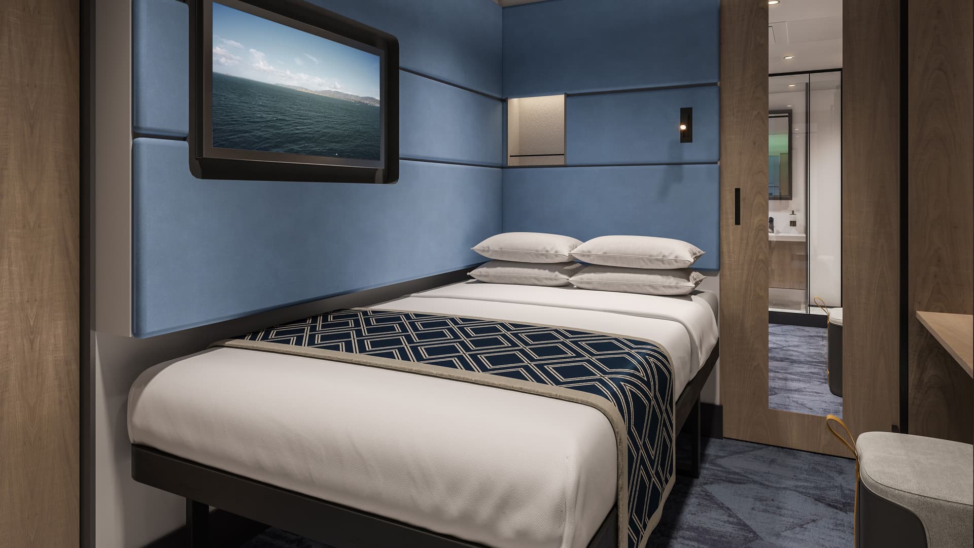 Solo Studio on Norwegian Aura with a bed, blue padded walls, a wall-mounted TV showing an ocean view and wood cabinetry.