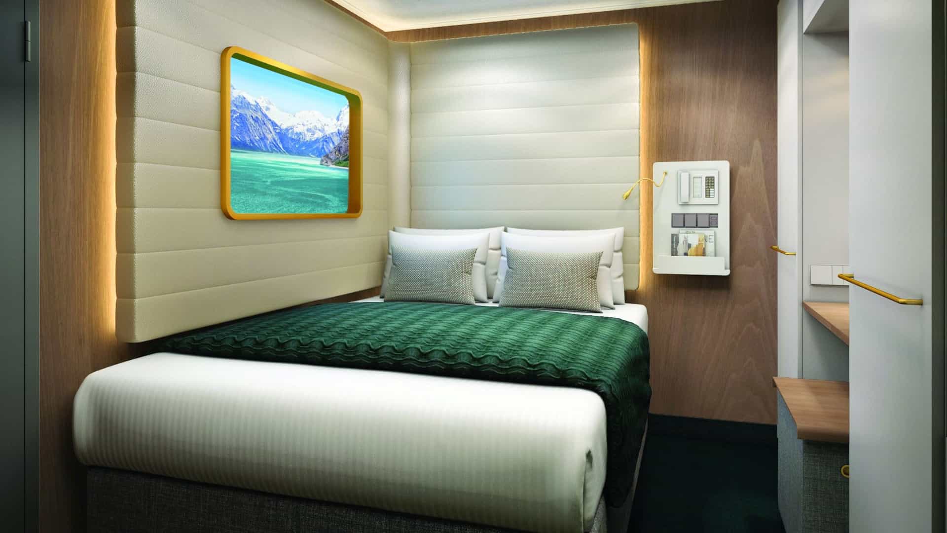 Studio on Norwegian Encore with a bed, green blanket, padded headboard and a framed wall screen showing a mountain scene.