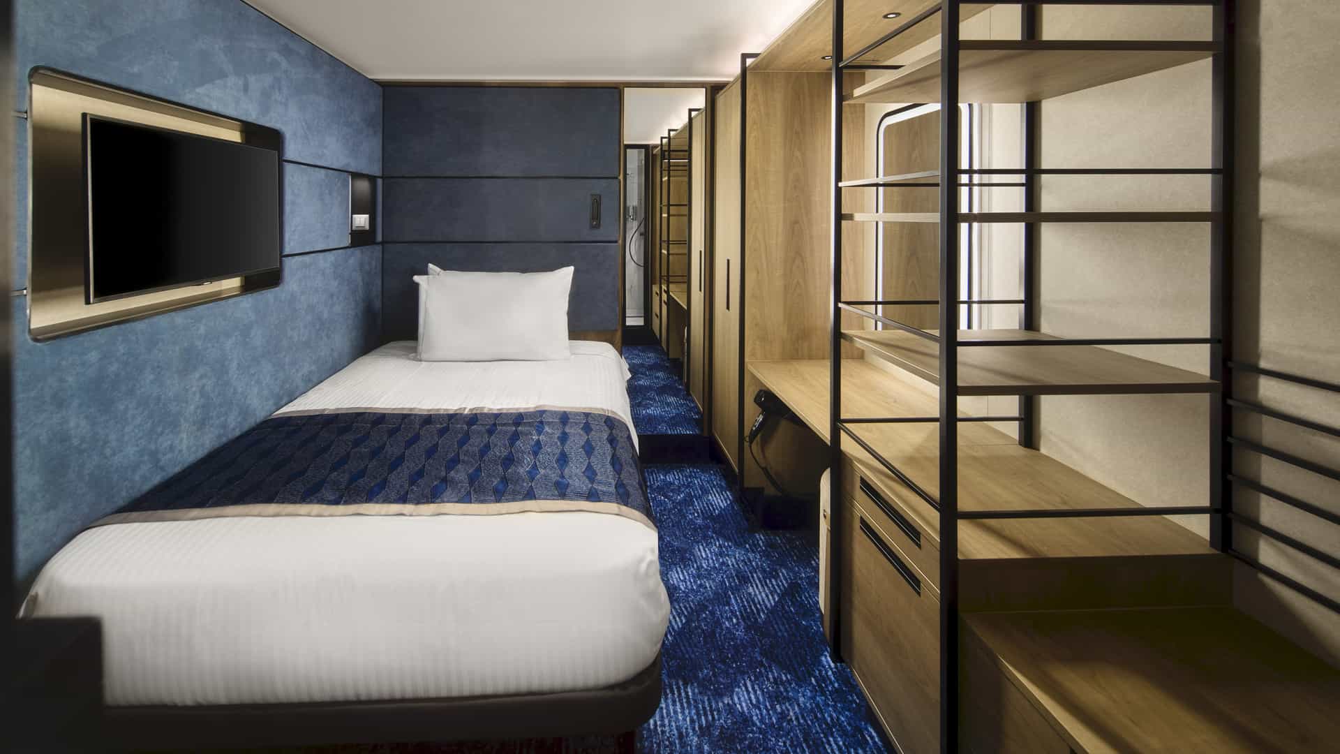 Solo Studio on Norwegian Prima with a single bed, blue wall, wall-mounted TV and open wood shelving.