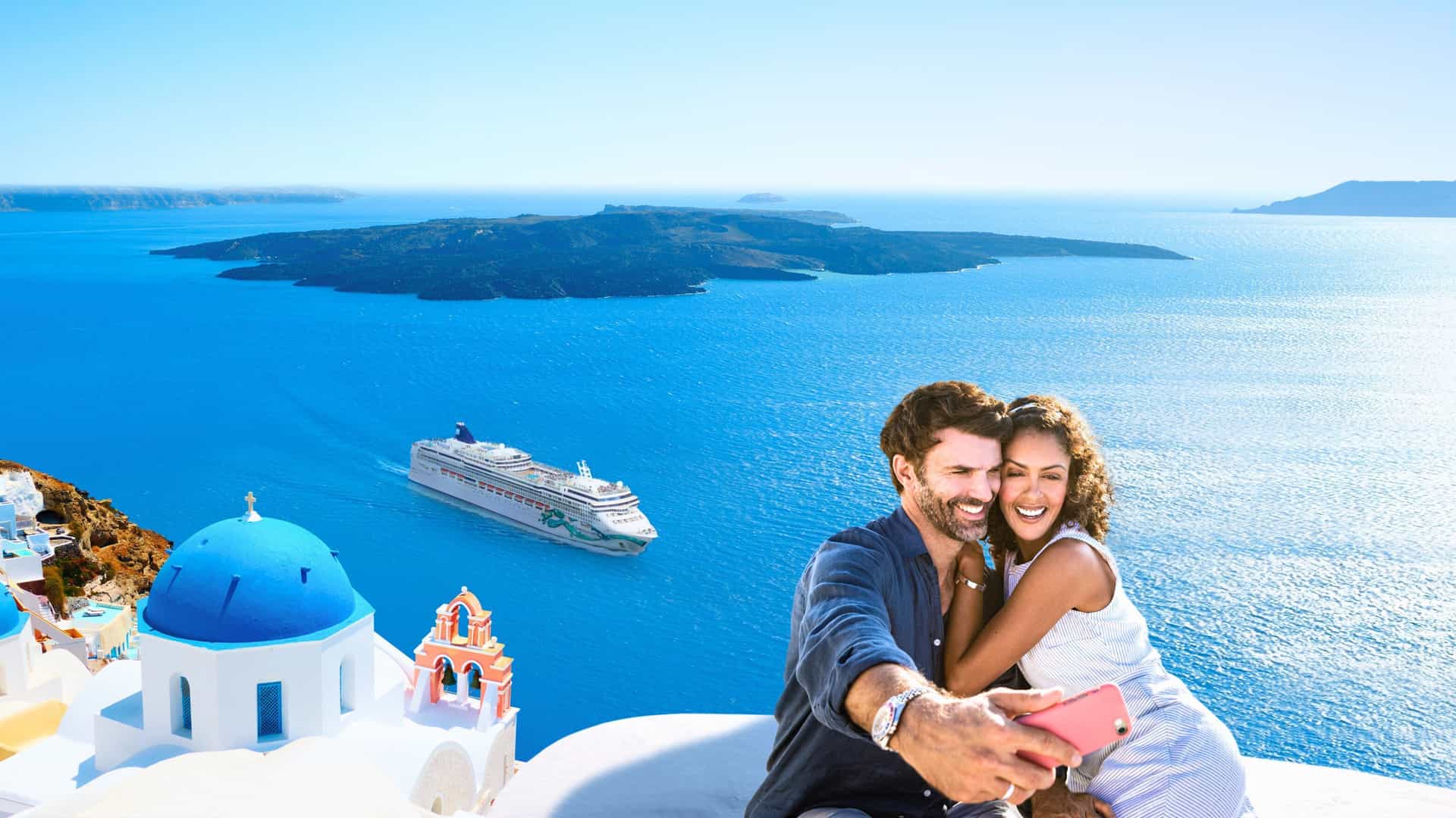 A couple takes a selfie with a scenic view of the blue domes of Santorini, Greece, and a Norwegian Cruise Line ship sailing in the caldera.