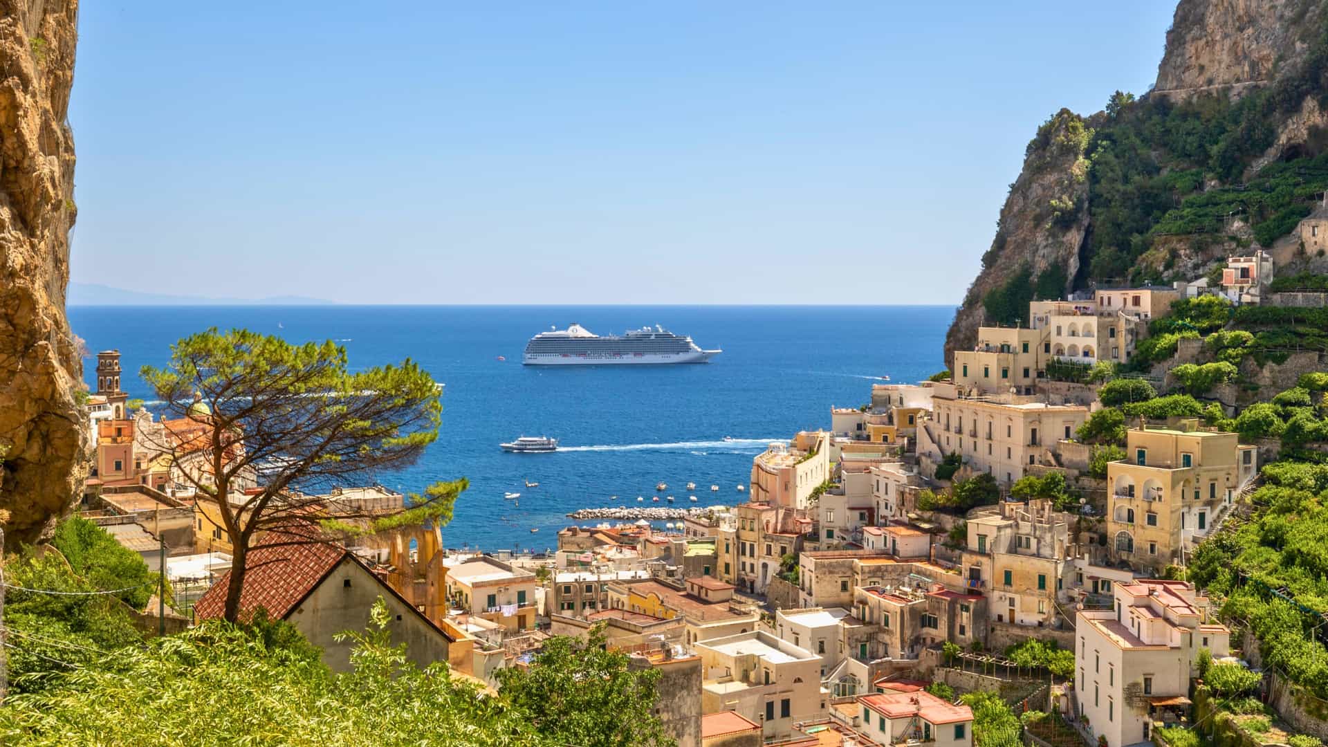 An Oceania Cruises ship sails past the picturesque Amalfi Coast in Italy, showcasing the stunning Mediterranean landscape, a beautiful stop on a European or World Cruise.