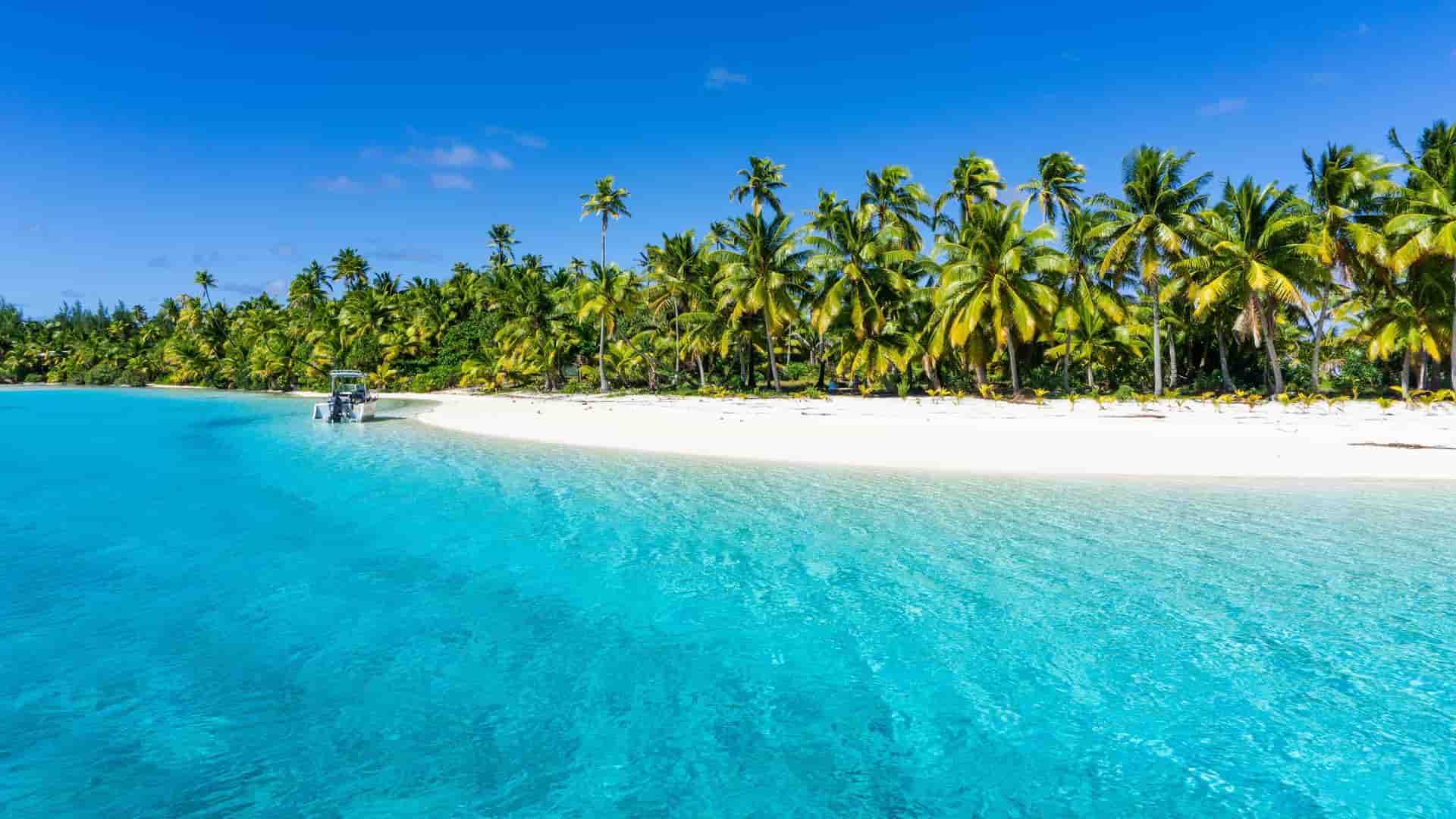 A tropical paradise on Aitutaki Island, with a pristine white sand beach lined with lush palm trees, and a small boat anchored in the crystal-clear turquoise water.