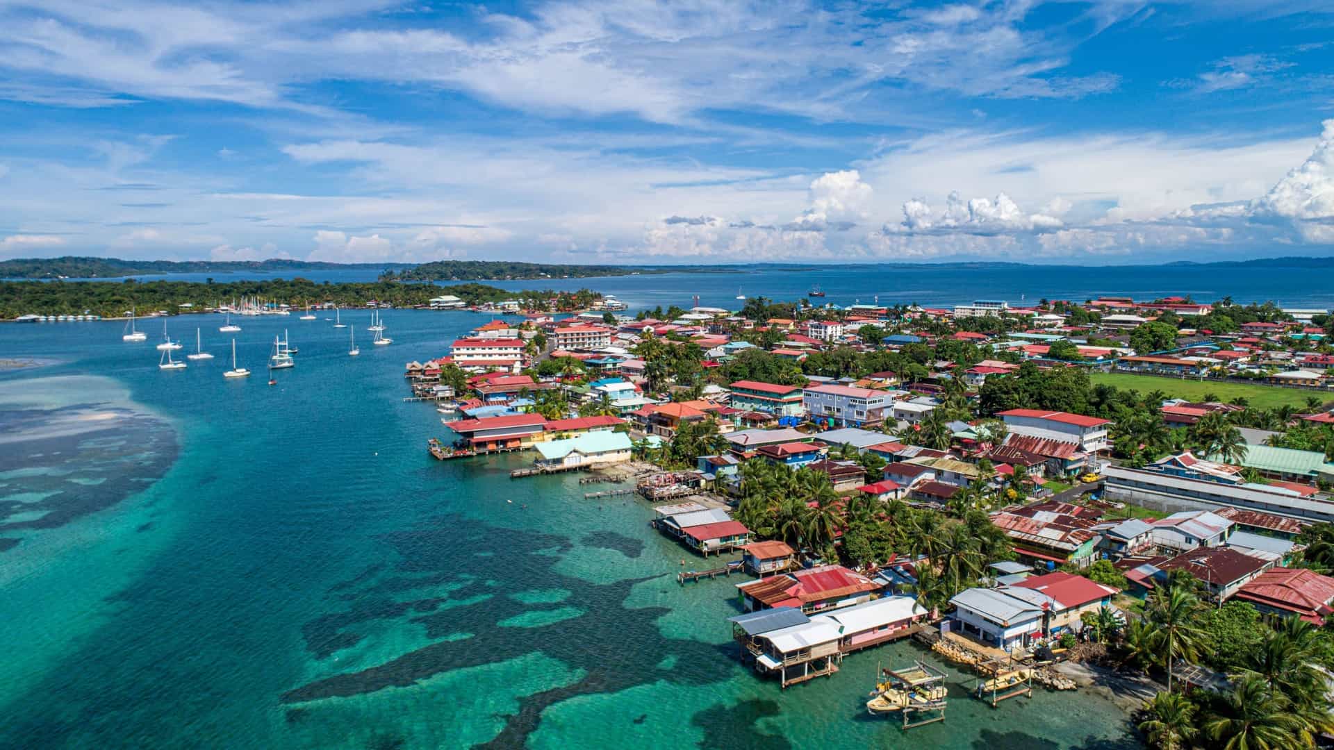 An aerial view of Bocas del Toro, a vibrant town on the Caribbean coast of Panama, featuring colorful houses built over clear blue water and numerous sailboats docked nearby.