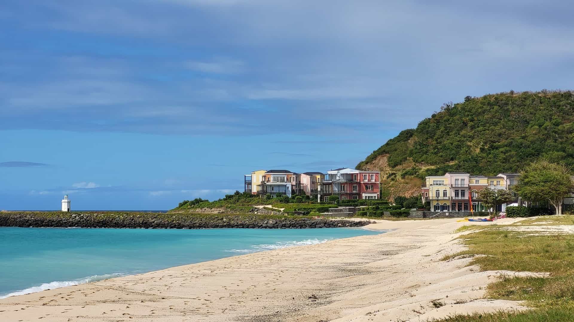 Brightly colored villas line a lush hill overlooking the white sand beach and turquoise sea of Canouan Island.