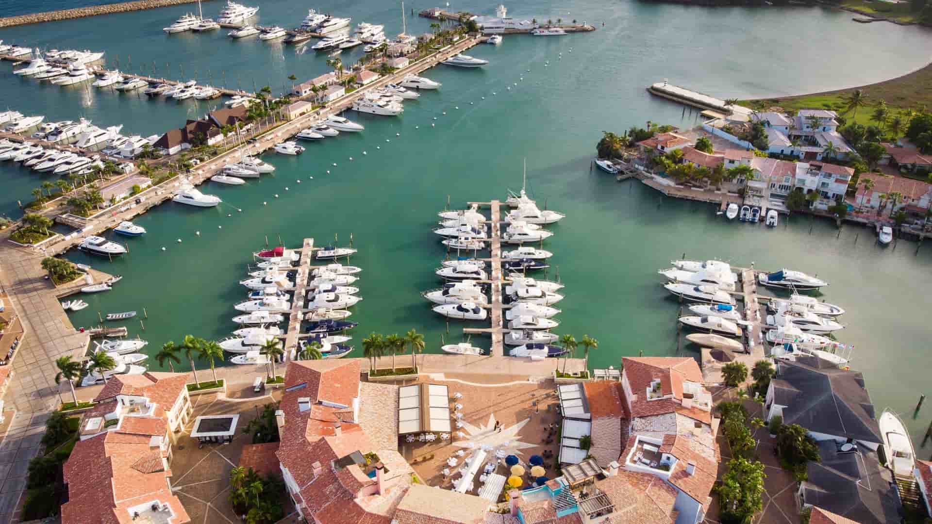 An aerial view of the Casa de Campo Marina in the Dominican Republic, showcasing luxury yachts docked in the harbor next to a village of elegant villas with red tile roofs.
