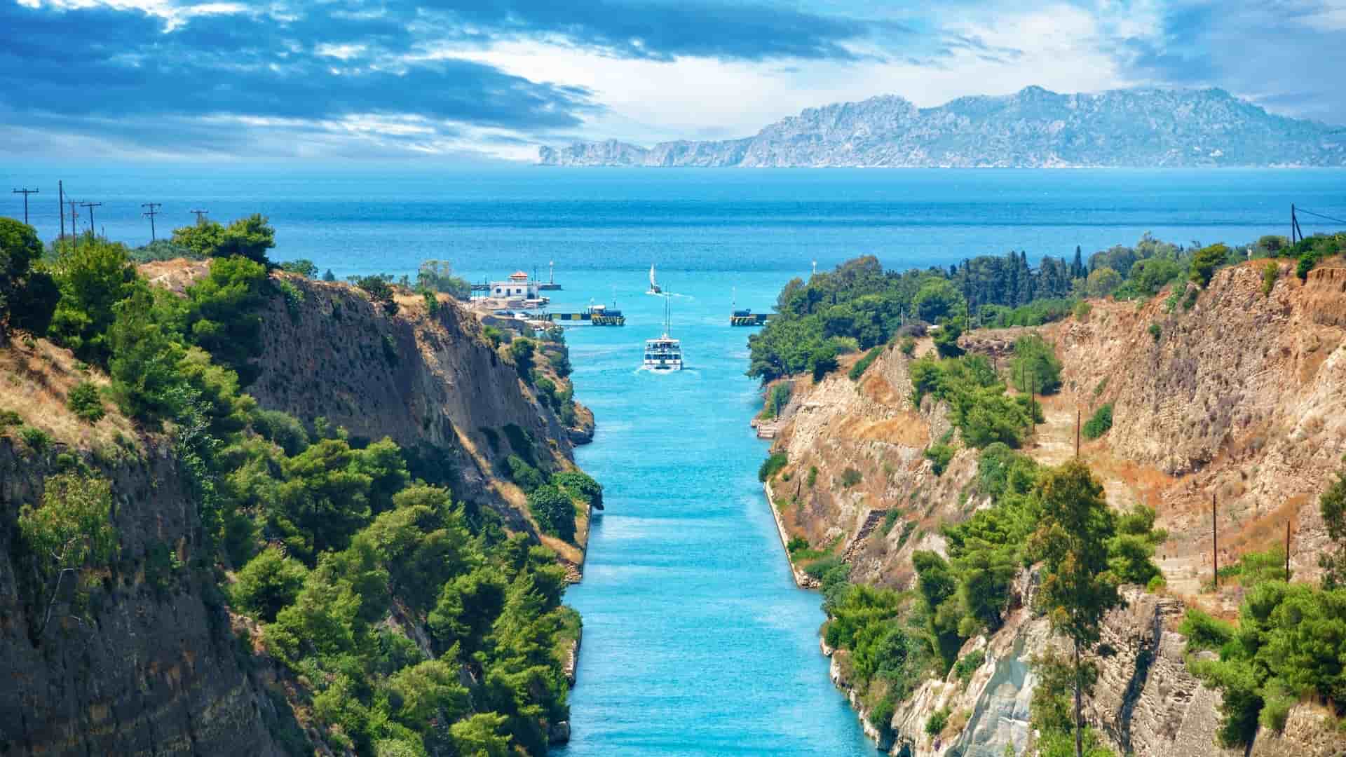 A stunning view of the Corinth Canal in Greece, with a tour boat navigating the narrow passage between the steep cliffs covered in lush vegetation.