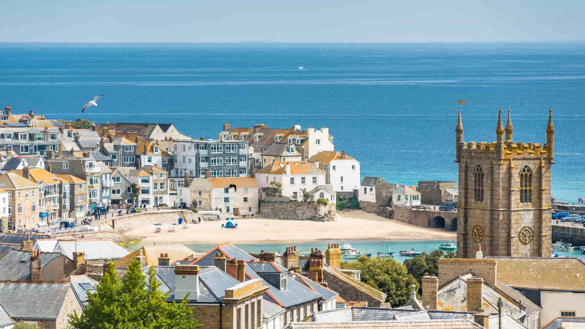 Scenic view of St. Ives coastal town in Cornwall, UK. St. Ia's Church tower overlooks the harbor beach and the blue Atlantic Ocean.