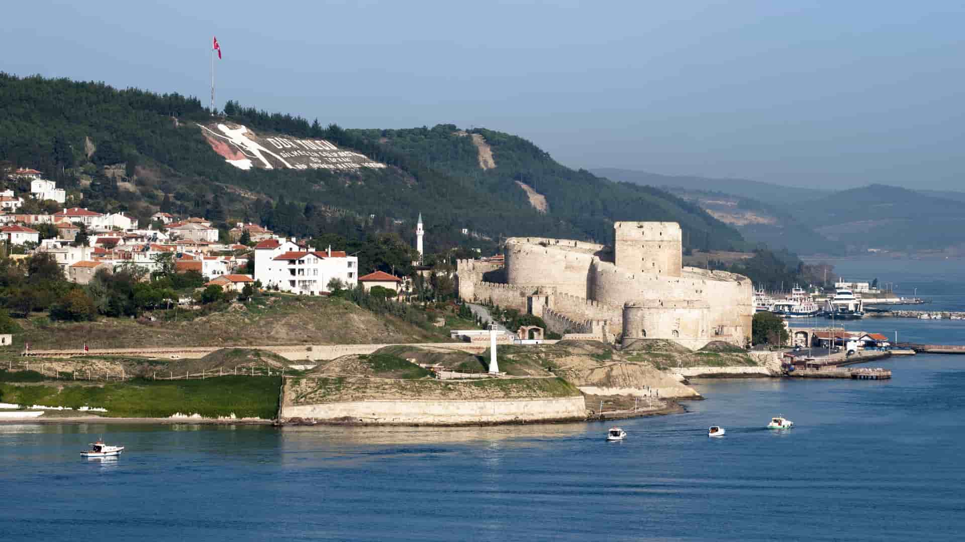 A scenic view of the historic Kilitbahir Castle fortress on the Dardanelles Strait in Turkey, situated on a hillside above a harbor and coastal town.