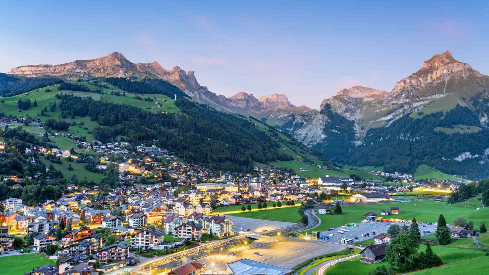 Illuminated alpine village of Engelberg, Switzerland, nestled in the valley beneath the towering peaks of the Uri Alps at dusk.