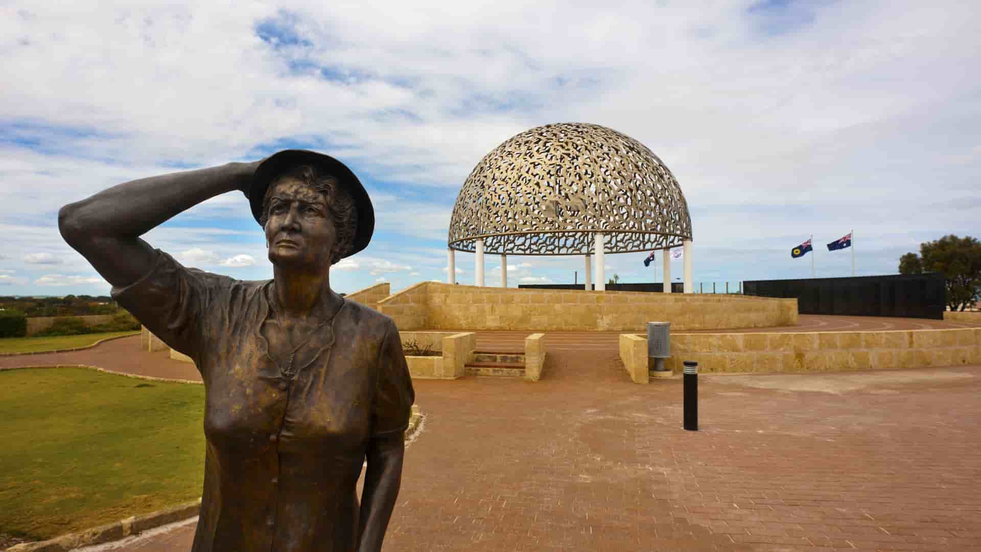 A close-up of the HMAS Sydney II Memorial in Geraldton, Australia, featuring the "Waiting Woman" bronze statue with the dome of 645 stainless steel seagulls in the background.