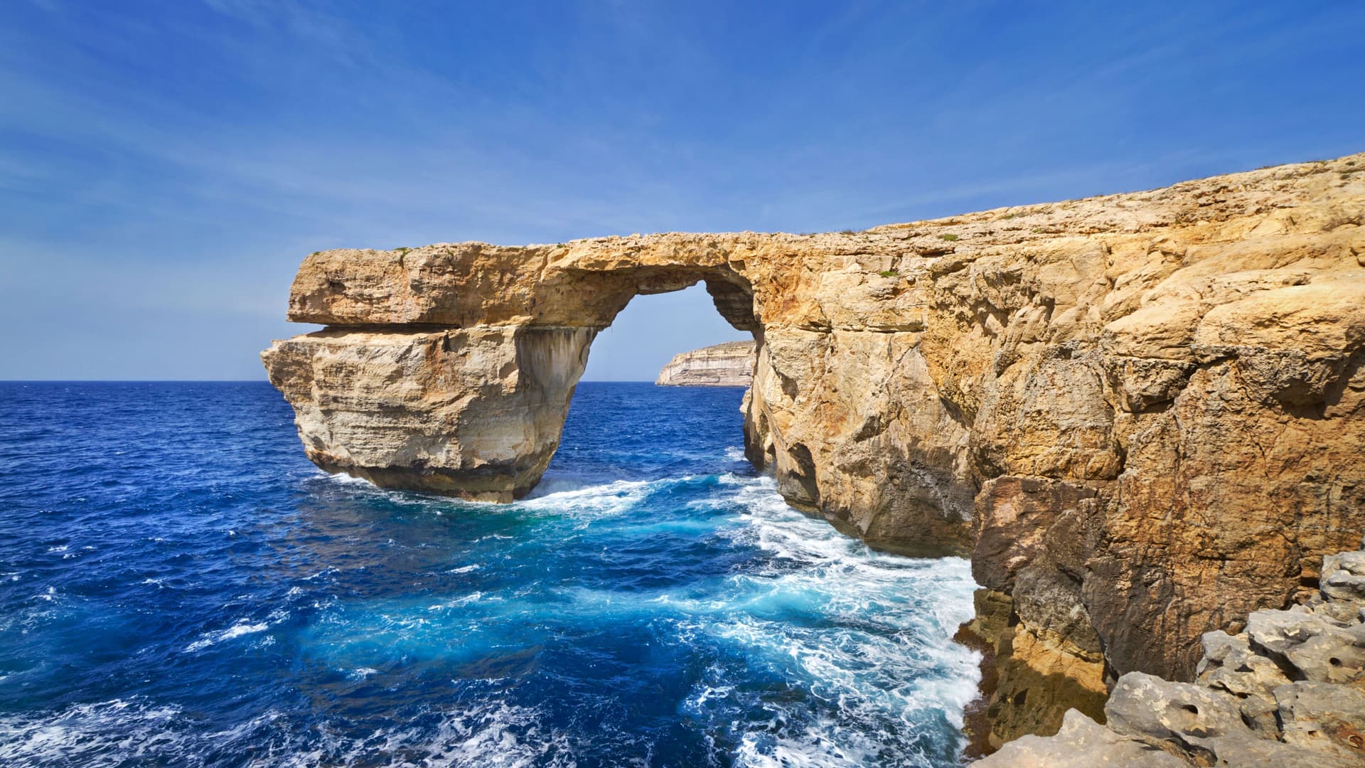 A beautiful landscape of the iconic Azure Window, a natural rock archway in Gozo, Malta, with powerful blue waves crashing below the massive cliffs.