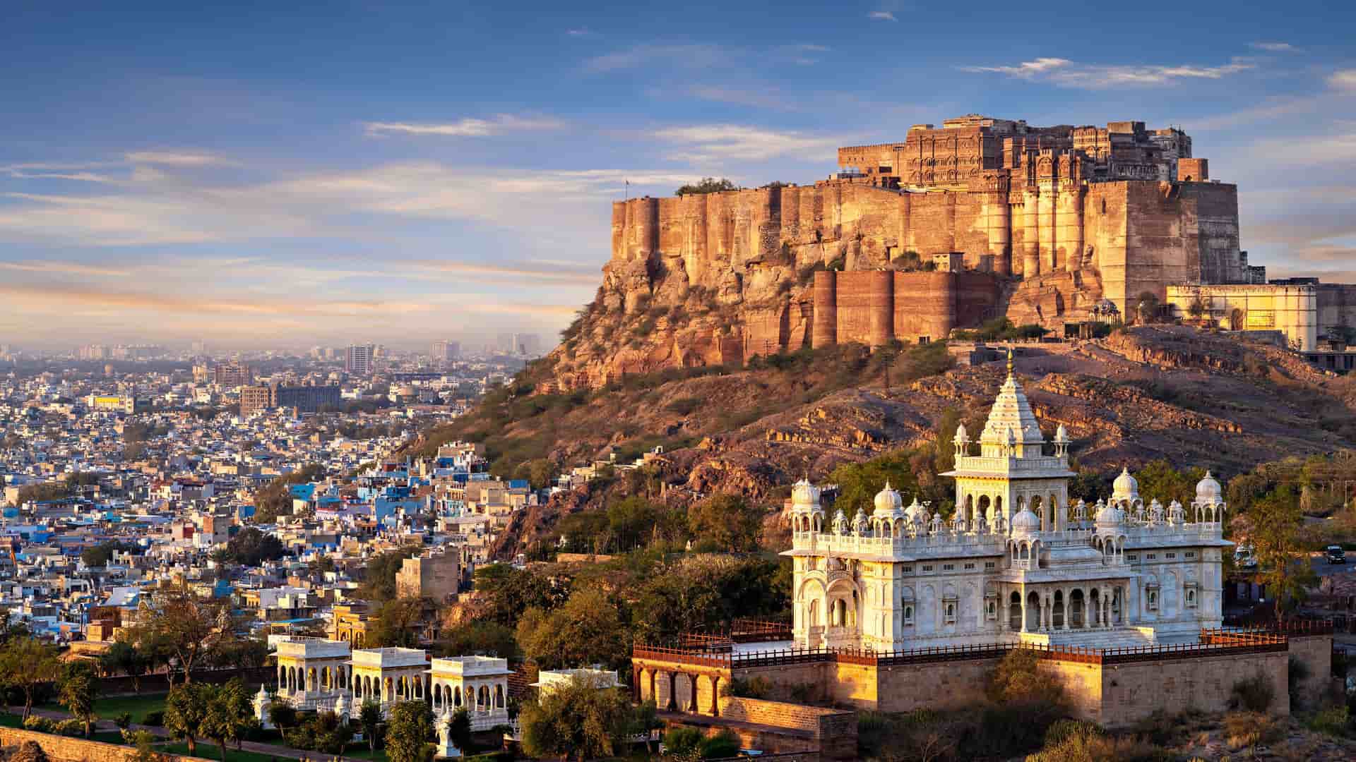 A breathtaking view of the Mehrangarh Fort towering over the city of Jodhpur, with the stunning white marble Jaswant Thada mausoleum in the foreground.